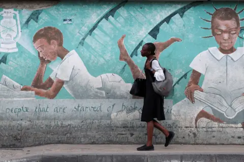 SODIQ ADELAKUN / REUTERS A girl walks past a wall painting depicting schoolgirls reading books. It is a tribute to schoolgirls who were abducted from their homes in Chibok a decade ago.