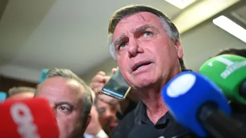 Jair Bolsonaro speaks to journalists on Tuesday, surrounded by red, blue and green microphones.