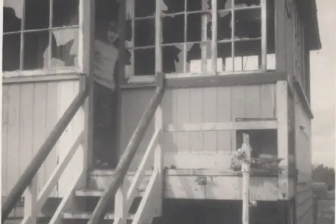 Paul Antell Collection A black and white photo shows a young Paul Antell standing in the doorway of a derelict wooden signal box with smashed windows.