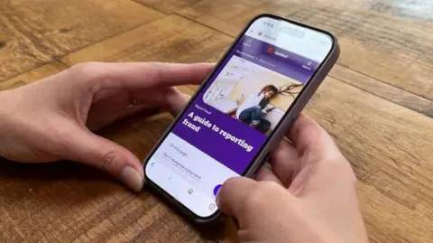 A view of Samantha looking at her phone, which shows the web page for reporting fraud to NatWest.