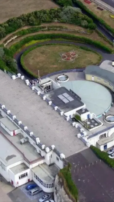 Aerial shot of large grey building on cliff edge