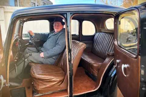 Callum in his car with the doors open so you can see inside