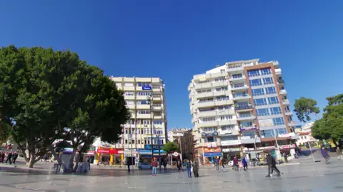 Google Street view of Cumhuriyet Street in Antalya. Cafe's and shops line the street and shoppers can be seen walking along the pavements.