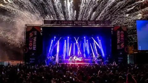 Godiva Festival's main stage, with lots of blue lights on a band and fireworks coming out of the top of the construction