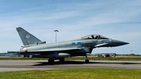 RAF Typhoon aircraft on a runway under a blue sky.