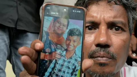 Getty Images Suresh Patni, father of Akash Patni, a victim of the Air India Flight 171 crash, shows a photograph of his wife (L) and deceased son