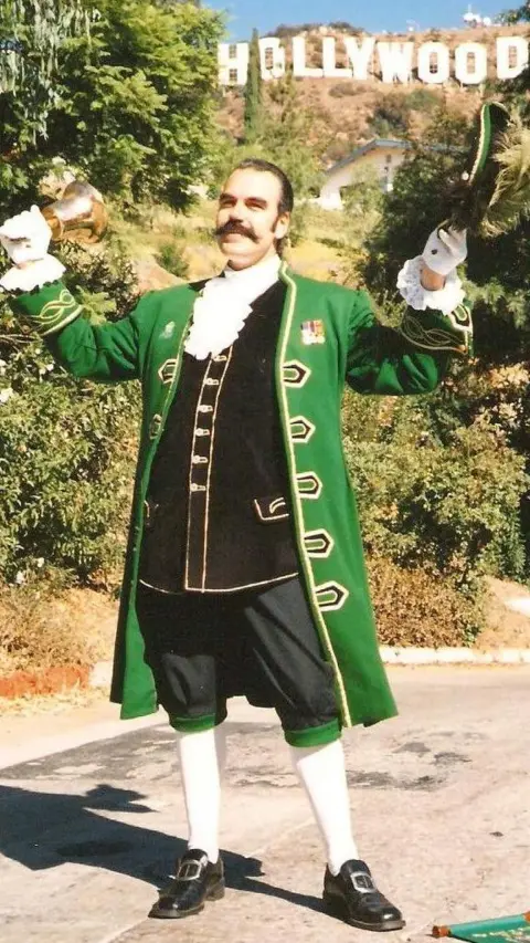 Michael Wood Michael Wood - a man in a green and black town crier uniform - with the famous Hollywood sign behind him