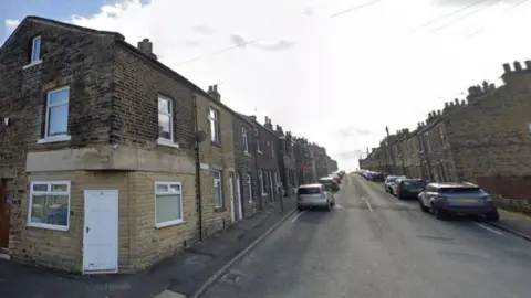 A street with a row of terraced houses on both sides with cars parked on the roadside.