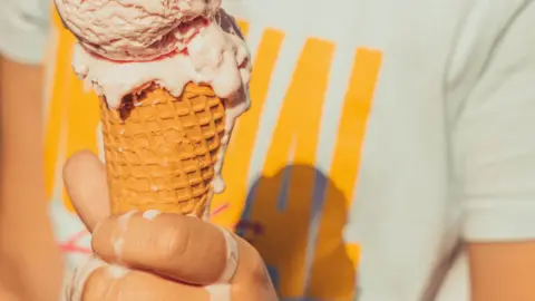 A hand holding an ice cream cone. The ice cream is melting onto the person's hand. 