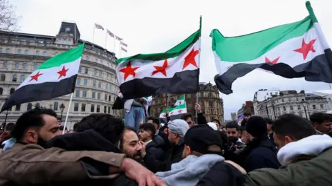 Reuters People wave Syrian opposition flags as they gather in Trafalgar Square, in London, on December 8, 2024