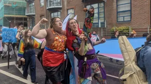 KIT TAYLOR/BBC People taking part in the parade, wearing outfits filled with different colours and patterns. One person with red hair holds up a skateboard.