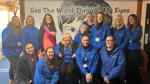 Supplied Ms Gane and a group of people from the Toby Henderson Trust pose for the camera. Ms Gane is in a pink ballgown. The rest of the group is wearing a blue uniform.