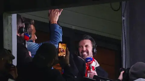 Getty Images Rob and Ryan celebrating after Wrexham score. They are high fiving each other, whilst holding their commentary microphones and wearing headphones. 
