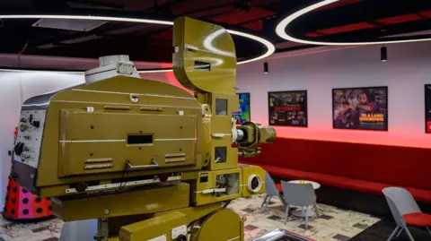 An old-fashioned video camera in an exhibition space filled with film posters