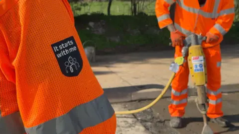 two men in a high vis holding a drilling device. there's a badge which says "it starts with me".