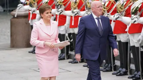 Getty Images Nicola Sturgeon in pink suit and Peter Murrell in blue suit walking past members of the Household Cavalry at an event for the Jubilee.