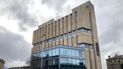 A rectangular-shaped concreted building with a glass frontage on one side.