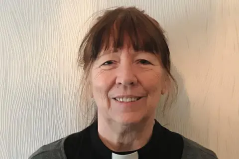 Annie Gray Head-and-shoulders image of Annie Gray. She is smiling as she looks directly into the camera. She has dark hair with a fringe. She is wearing a cleric's dog collar.