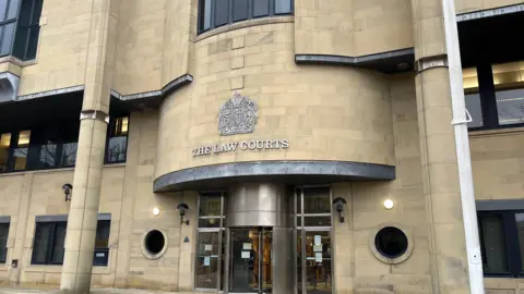 The outside of Bradford Crown Court - a bland-looking grey building with a silver revolving door.