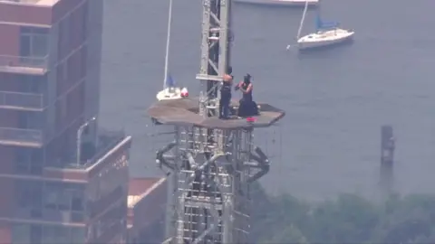 A man and a woman are seen during a proposal on top of the top of the Empire State Building.
