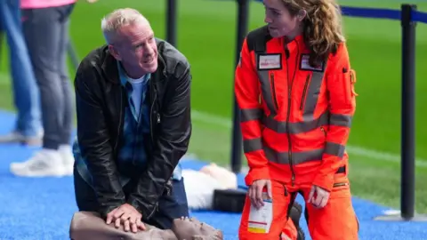 Fatboy Slim being taught how to do CPR at Amex Stadium in Falmer 