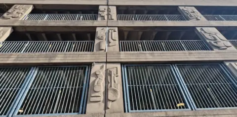 North East Lincolnshire Council 10 concrete pillars adorned with abstract designs that protrude from the concrete panels. In between the pillars are railings.