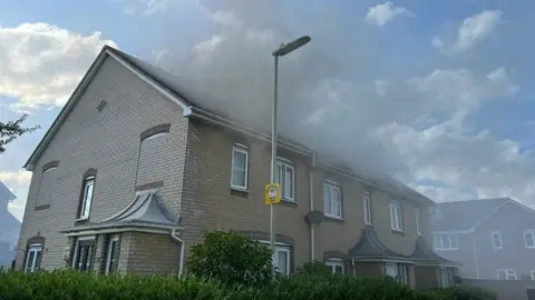 HIWFRS Smoke billowing from the roof at the front of a pale brick, terraced home with white windows