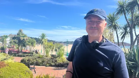 Man with blue cap in front of beach gardens 