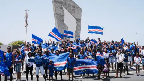 Michel Mvondo/BBC A group of fans, wearing the blue national kit, wave Cape Verde flags.