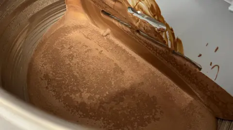 Tom Jackson/BBC A silver barrel has chocolate at the bottom which has been melted and reset. It only fills a small portion of the barrel.