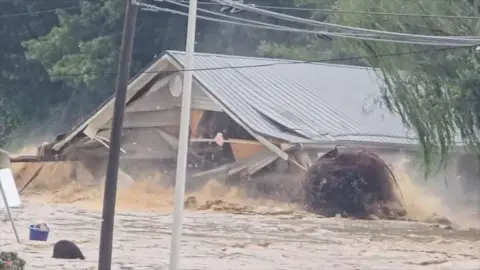 A house floats down a muddy river collapsing