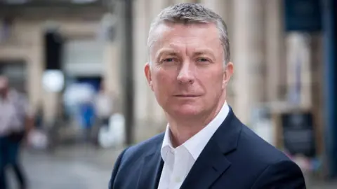 North East Chamber of Commerce A man with grey hair is wearing a white shirt and dark blue suit jacket