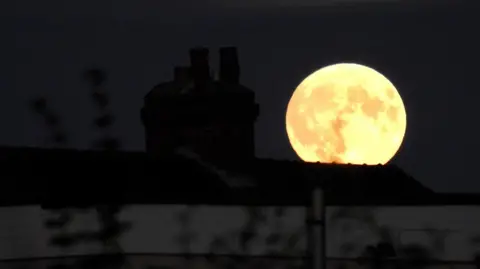 BBC Weather Watchers/Stevie T A yellow moon glows above the dark shadow of a house in Wakefield.