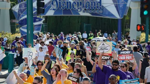 Getty Images Hundreds of Disneyland workers are seen with signs protesting outside the park's gates 