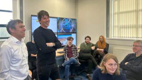 BBC Students and teachers gathered around Prof Brian Cox as he speaks to them.