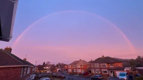 BBC Weather Watchers/Ramshots A large rainbow hangs over a housing estate on a winter's morning, with a pinky-blue sunrise lighting up the clear sky.