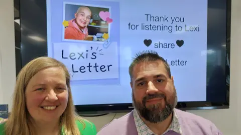 Supplied Lexi's parents, Liz and Andy, sat together in front of a screen with Lexi's letter