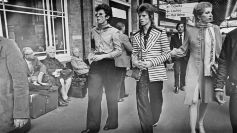 Getty Images British fashion designer Anthony Price (L) with David Bowie (C) and his wife Angie Bowie at King's Cross station in London in 1973.