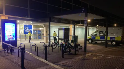 A police cordon outside the entrance to the Centre:MK. There are two police officers in yellow high vis jackets and a police van. 