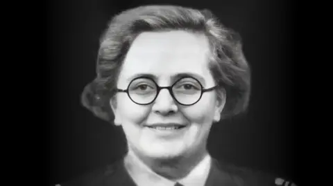 Jeff Harrison Flight Captain Susan Slade in black and white. She has short, combed back hair, round dark glasses and is slightly smiling. The collar of her shirt and jacket can be seen.