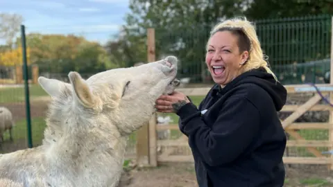 Lauren Carter/BBC A smiling Jodie Marsh looking directly at the camera and petting an animal in a paddock