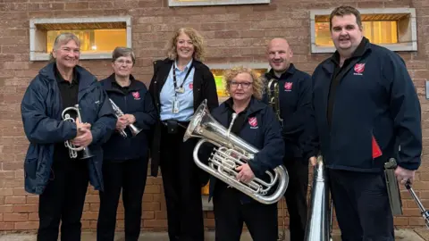 Salvation Army Salvation Army band outside a prison. There are six band members, most who are holding brass instruments 