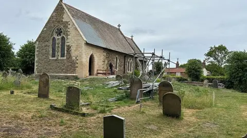 The South Wolds Partnership The newly repaired church seen from the graveyard. It has new light-coloured stone work with a new doorway and scaffolding nearby 