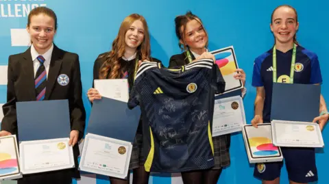 Robert Perry Four school girls holding up certificate awards and a signed Scotland football shirt, while all grinning broadly