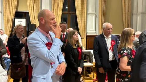Labour supporters and councillors wearing red rosettes and looking sombre.