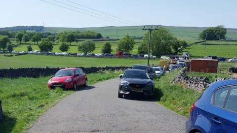 Cars parked on a road with green fields either side
