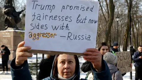 EPA Protester in Kyiv on 26 February 2025 holds up sign saying "Trump promised fairness but now sides with aggressor - Russia"