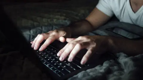 As imagens getty são um homem incontrolável, deitado na cama e usando um laptop