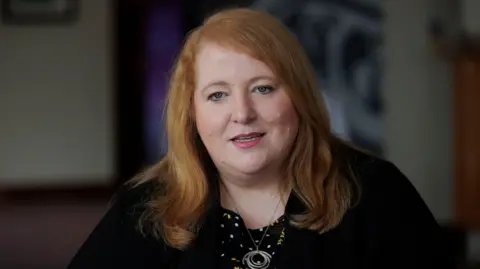 Liam McBurney/PA Wire Justice Minister Naomi Long looking to camera, wearing a achromatic  jacket, a black, achromatic  and yellowish  apical  with polka dots and floral patterns, and a necklace with concentric rings. 