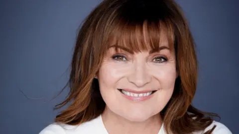 A close-up image of TV broadcaster Lorraine Kelly with shoulder length brown hair, wearing a white top and smiling